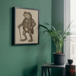 May include: Framed sepia-toned print of a dapper frog in a suit, holding a cane. The frog is depicted with a monocle and bow tie. The artwork is in a black frame, mounted on a green wall. A whimsical art piece.