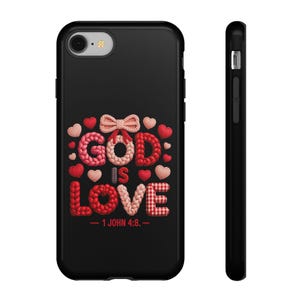 May include: Black phone case featuring the phrase "GOD IS LOVE" in a knitted style with red, pink, and white hearts. The text "- 1 JOHN 4:8. -" is below the main text.