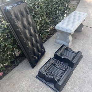 Puede incluir: Moldes negros de plástico para jardineras y un banco de hormigón gris se exhiben sobre una superficie de hormigón. Los moldes tienen diseños decorativos y un diseño acolchado. El banco tiene un patrón acolchado en el asiento.