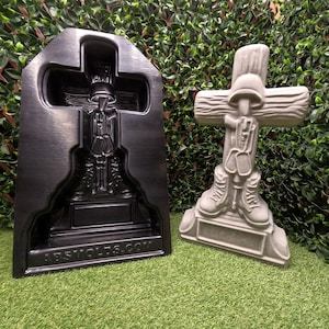 Puede incluir: Una estatua de cruz de hormigón gris con un casco de soldado, chapas de identificación y botas. Junto a ella, un molde negro con el mismo diseño de cruz de soldado. El molde tiene el texto "ABS MOLDS.COM".