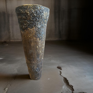 Könnte beinhalten: Eine hohe, keramische Vase mit einer strukturierten, dunkelbraunen und goldenen Oberfläche. Die Vase hat eine breite Öffnung oben und verjüngt sich nach unten zu einer schmalen Basis.