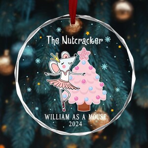 May include: A clear glass Christmas ornament with a ballerina mouse illustration. The ornament features a pink and blue Christmas tree with a star on top. The text "The Nutcracker" is at the top of the ornament and "William as a Mouse 2024" is at the bottom.