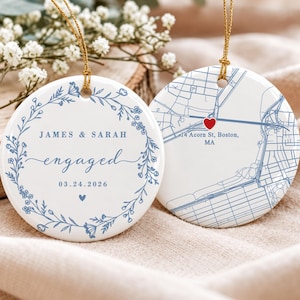 May include: Two round white ceramic ornaments with gold hanging strings. One features a blue floral wreath, the text JAMES & SARAH, engaged, and 03.24.2026. The other displays a blue street map of 14 Acorn St, Boston, MA with a red heart icon.