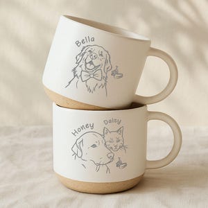 May include: Two stacked white ceramic mugs with tan bases and handles. Each mug features a line drawing of a pet with a name above it. The top mug has a dog named Bella wearing a bow tie. The bottom mug has a dog named Honey and a cat named Daisy.