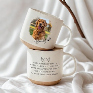 May include: Two stacked white ceramic mugs. The top mug features a photo of a golden retriever, the name "Bailey", and paw prints. The bottom mug has a quote about remembrance and an angel wing graphic.