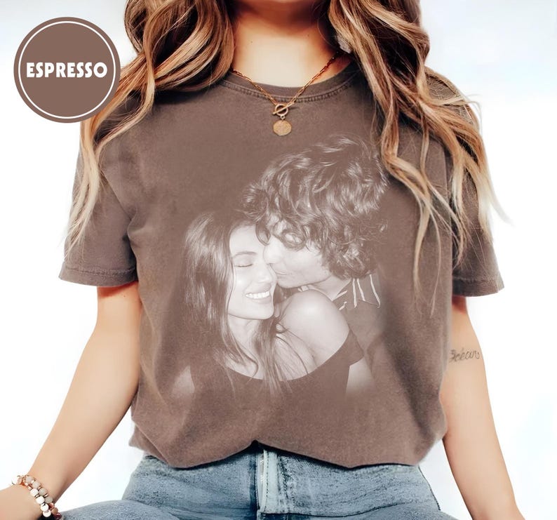May include: Espresso-coloured t-shirt with a black and white image of a couple. The t-shirt has a crew neck and short sleeves. The word "ESPRESSO" is in a brown circle in the upper left corner.
