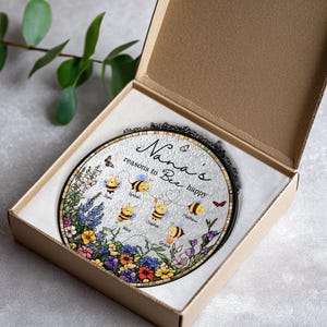 May include: A round, decorative glass piece in a gift box. The glass features a floral and bee design with the text "Nana's reasons to Bee happy" and names. The piece is framed in black and comes in a brown cardboard box.