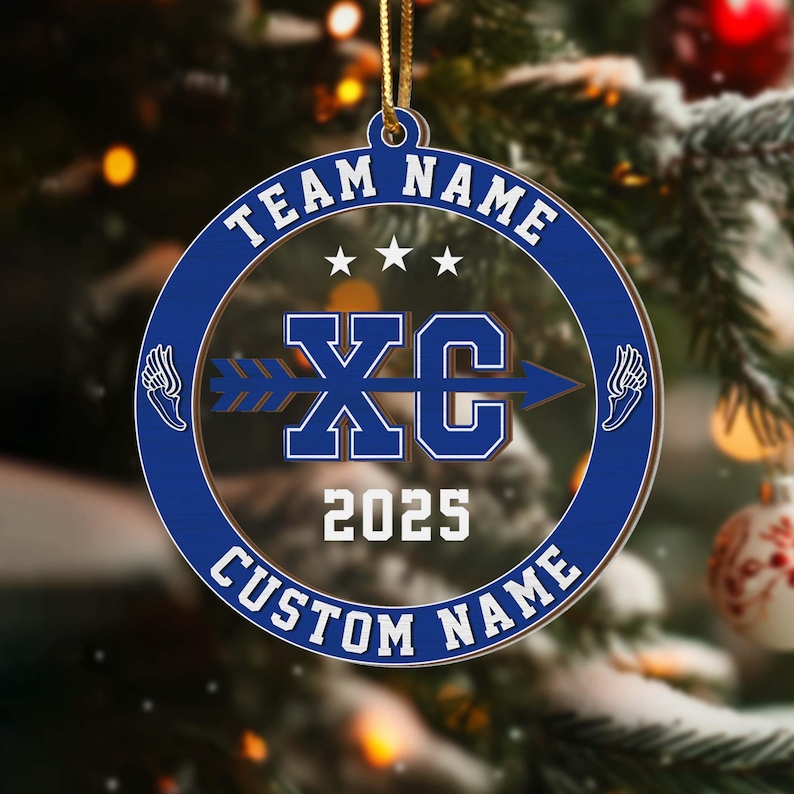 Puede incluir: Un adorno circular azul y transparente con el texto "TEAM NAME" y "CUSTOM NAME" en blanco. El centro presenta "XC" con una flecha, el a&ntilde;o "2025" y gr&aacute;ficos de alas. El adorno cuelga de una cuerda dorada.