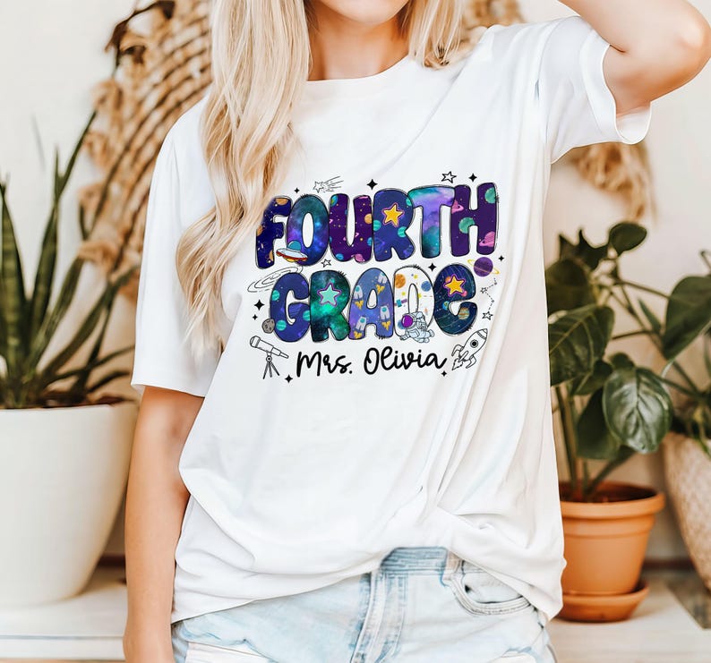 May include: White t-shirt with a colorful "FOURTH GRADE" graphic in a space theme, including stars, planets, and a rocket. The text "Mrs. Olivia" is printed below the main design.