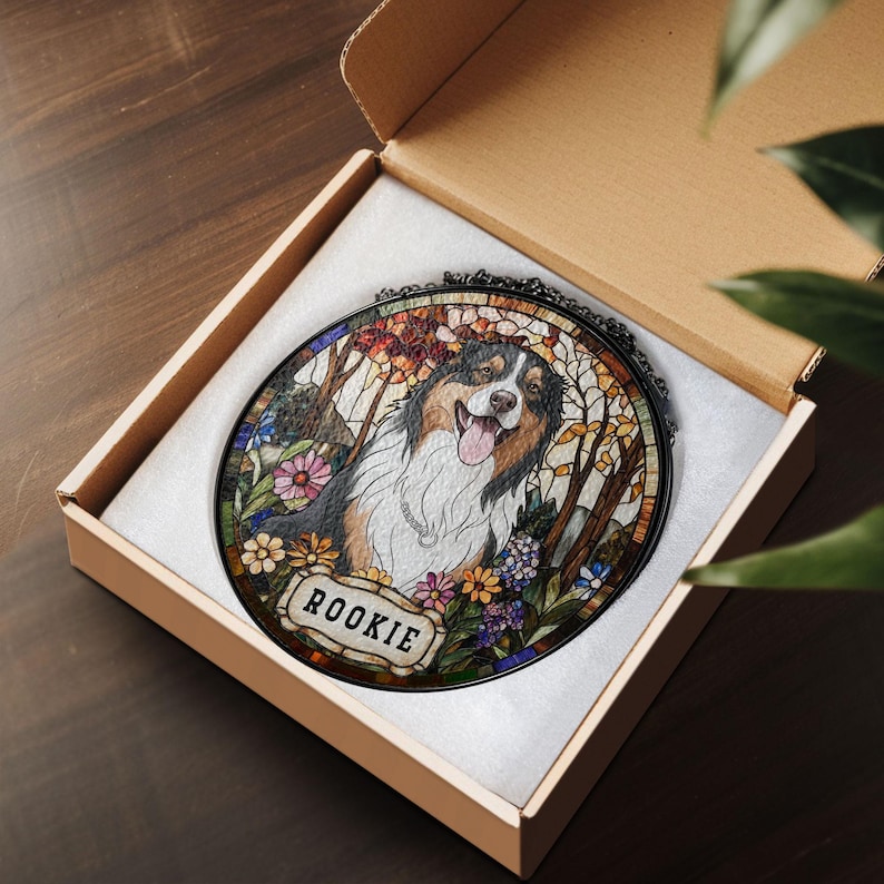 May include: A stained glass-style portrait of a dog with a happy expression, surrounded by flowers and trees. The dog's name, "ROOKIE," is displayed on a small banner. The artwork is presented in a cardboard box.