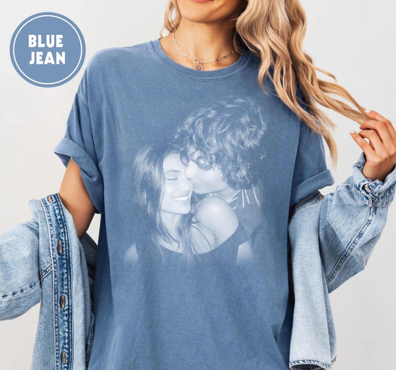 May include: A blue jean-coloured t-shirt with a black and white image of a kissing couple. The shirt has rolled-up sleeves and the words "BLUE JEAN" in a blue circle. A denim jacket is draped over the arm.