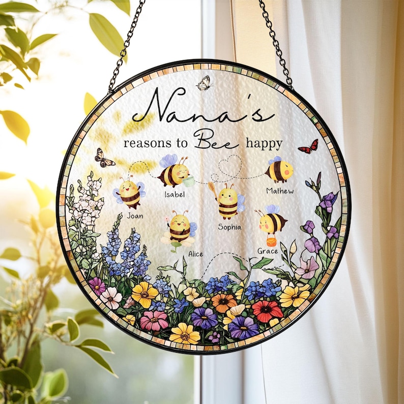 May include: Round stained glass window art with a black metal frame and hanging chain. The design features the text "Nana's reasons to Bee happy" with cartoon bees and names. Colorful flowers and butterflies decorate the border.