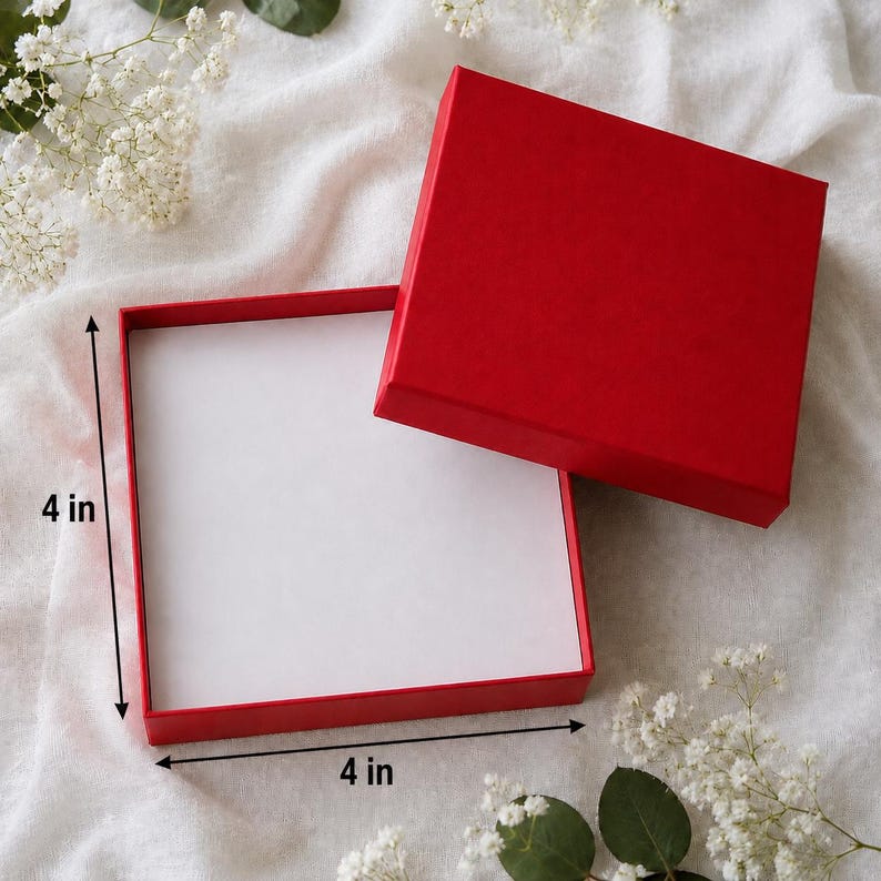 May include: A square red gift box with a removable lid, featuring a white interior. The box measures 4 inches by 4 inches as indicated by the black arrows and text labels on the image, providing a clear visual reference for its dimensions.