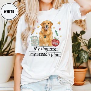 Puede incluir: Una camiseta blanca con un gr&aacute;fico de un perro golden retriever, una manzana roja con el nombre Ozzy, un l&aacute;piz, un cray&oacute;n verde, estrellas y un documento de plan de lecci&oacute;n azul. El texto dice My dog ate my lesson plan en letras negras.