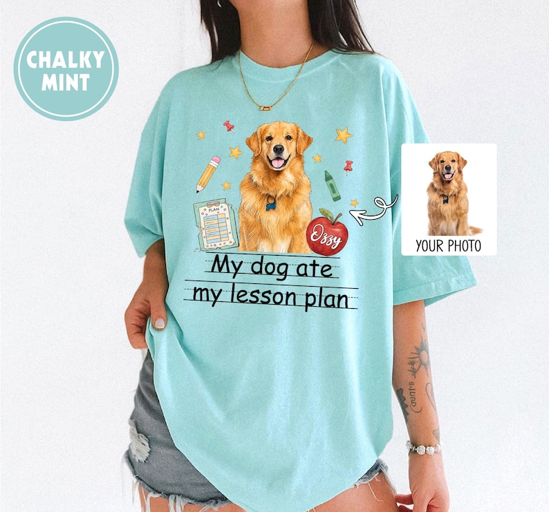 Puede incluir: Una camiseta azul claro con un gr&aacute;fico de un perro golden retriever, una manzana roja con el nombre Ossy, un l&aacute;piz, un cray&oacute;n y un documento de plan de lecci&oacute;n. El texto My dog ate my lesson plan est&aacute; impreso en negro bajo el perro.