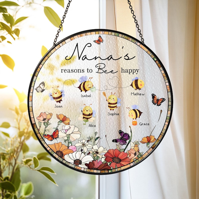 May include: Round stained glass window art with the text "Nana's reasons to Bee happy". The design features cartoon bees, butterflies, and flowers. The names Joan, Isabel, Mathew, Sophia, Alice, and Grace are included.