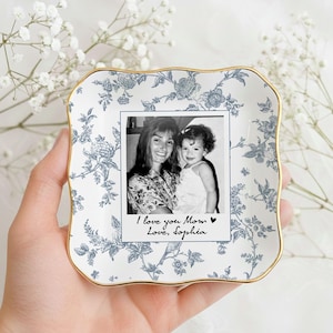 May include: A square, white ceramic trinket dish with a blue floral pattern and gold trim. The dish holds a black and white photo with the text "I love you Mom Love, Sophia."