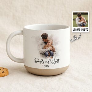 May include: White ceramic mug with a brown base and handle. The mug features a watercolor-style image of a father and child, with the text "Daddy and Wyatt 2026". A small photo with "UPLOAD PHOTO" text is also visible.