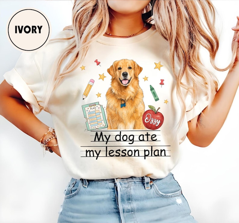 Puede incluir: Una camiseta de color marfil con un gr&aacute;fico de un perro golden retriever rodeado de material escolar, como un l&aacute;piz, un cray&oacute;n verde, un portapapeles y una manzana roja con la etiqueta Ozzy. El texto dice My dog ate my lesson plan.