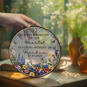 May include: A round memorial plaque with the text "ALWAYS & FOREVER IN OUR Hearts" and "IN LOVING MEMORY OF Grandma 25.05.2025". The plaque features a floral border with butterflies and a heart.