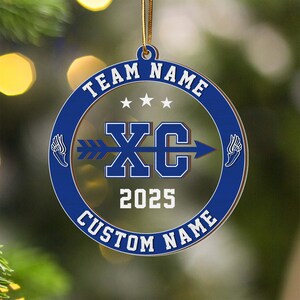 Puede incluir: Adorno redondo, azul y transparente, con los textos blancos &laquo;&nbsp;TEAM NAME&nbsp;&raquo; y &laquo;&nbsp;CUSTOM NAME&nbsp;&raquo;. El centro presenta &laquo;&nbsp;XC&nbsp;&raquo; con una flecha, el a&ntilde;o &laquo;&nbsp;2025&nbsp;&raquo; y gr&aacute;ficos de alas. Una cuerda dorada est&aacute; unida para colgar.