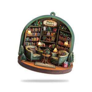 May include: A decorative ornament shaped like a dome featuring a miniature bookstore interior. It includes two green patterned armchairs, a small round table, bookshelves filled with books, and a sign that reads Amelia's Bookstore.