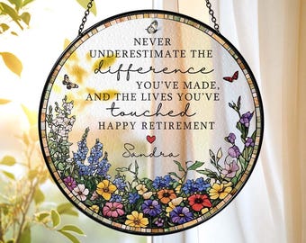 May include: Round, stained glass retirement gift with a black metal frame and hanging chain. The glass features a floral border with colorful flowers and butterflies. Text reads "Never underestimate the difference you've made... Happy Retirement Sandra."