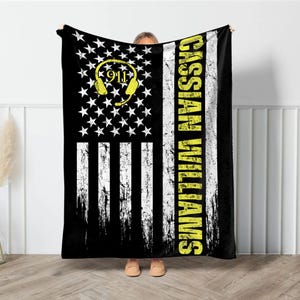 May include: A black and white American flag with a yellow distressed text that reads "CASSIA WILLIAMS" and a yellow 911 headset graphic.