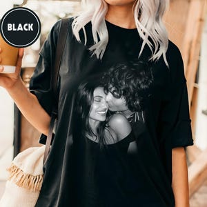 May include: Black oversized t-shirt with a black and white image of a couple kissing. The t-shirt has a round neckline and short sleeves. A black circle with the word "BLACK" is in the upper left corner.