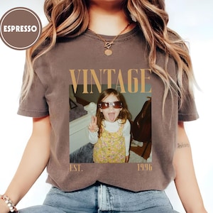 Puede incluir: Camiseta color espresso con un dise&ntilde;o vintage. La camiseta presenta una foto de un ni&ntilde;o con gafas de sol y sacando la lengua, con la palabra "VINTAGE" encima de la foto y "EST. 1996" debajo.