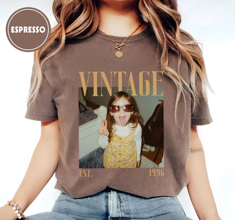 Puede incluir: Camiseta color espresso con un dise&ntilde;o vintage. La camiseta presenta una foto de un ni&ntilde;o con gafas de sol y sacando la lengua, con la palabra "VINTAGE" encima de la foto y "EST. 1996" debajo.