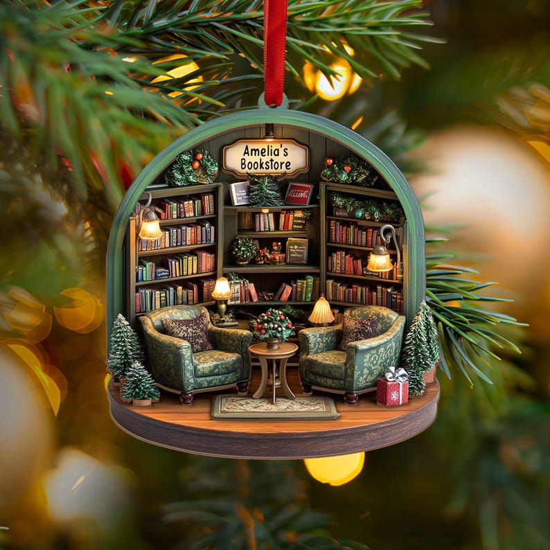 May include: A round, hanging Christmas ornament featuring a detailed miniature bookstore interior with two green patterned armchairs, a small center table, and bookshelves filled with books. A sign above reads Amelia's Bookstore.