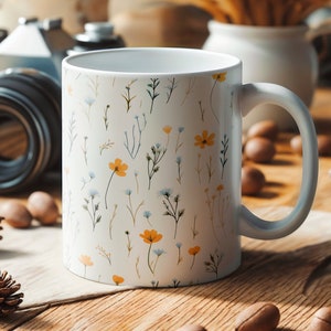 A mug with a dainty floral design with blue, yellow, and white flowers. The main color of the mug is white on the inside and outside.