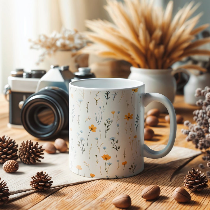 A mug with a dainty floral design with blue, yellow, and white flowers. The main color of the mug is white on the inside and outside.