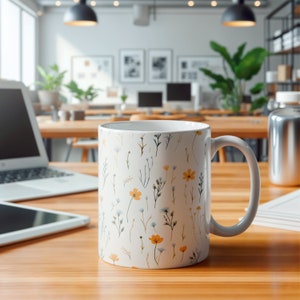 A mug with a dainty floral design with blue, yellow, and white flowers. The main color of the mug is white on the inside and outside.