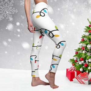 May include: White leggings with a repeating pattern of colorful Christmas lights. The lights are strung together with a black wire.