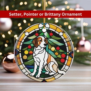 May include: A round Christmas ornament featuring a dog, possibly a Setter, Pointer, or Brittany, in a stained-glass style design. The ornament has a white background with a brown and white dog, surrounded by a green Christmas tree and red ornaments. The text "Setter, Pointer or Brittany Ornament" is at the top.