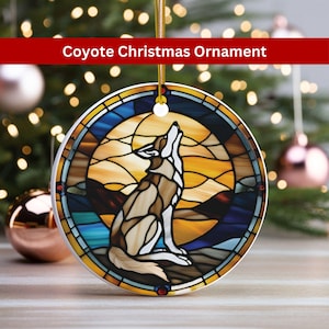 May include: A round ceramic Christmas ornament featuring a stained glass design of a coyote howling at the moon. The background is a sunset with blue and orange hues.