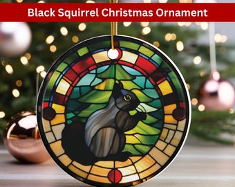 May include: A round ceramic Christmas ornament featuring a stained glass design of a black squirrel in a forest setting. The ornament has a gold string for hanging.