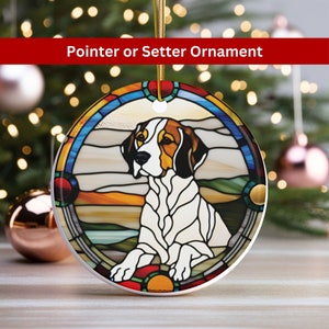 May include: A round ceramic ornament with a stained glass design of a white and brown dog with a black nose. The dog is sitting with its head turned to the side. The background is a colorful landscape with blue, green, orange, and yellow hues.
