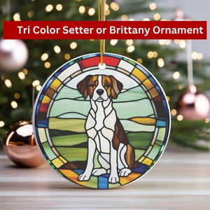 May include: A round, white ceramic ornament with a stained glass design of a tri-color setter dog sitting in a field. The ornament has a gold string for hanging.