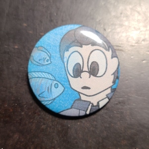 May include: A blue button with a cartoon illustration of a person with large eyes looking at three fish swimming in a blue background.