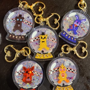 Puede incluir: Cinco esferas de nieve de vidrio transparente con llaveros dorados. Cada esfera presenta un personaje diferente de la serie de videojuegos Five Nights at Freddy's. Los personajes son Freddy Fazbear, Bonnie el Conejo, Chica la Gallina, Foxy el Zorro Pirata y Golden Freddy.