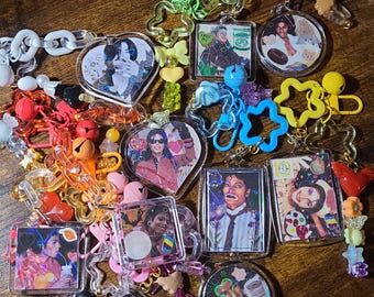 May include: A collection of acrylic keychains featuring various portraits of Michael Jackson. The keychains are attached to colorful plastic chains, star-shaped clasps, and assorted beads in shapes like hearts, flowers, and bears in vibrant colors.