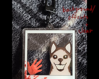 May include: A clear acrylic keychain featuring a cartoon image of a smiling husky with red blood splatter around the edges. The image is set in a white frame with a black background.