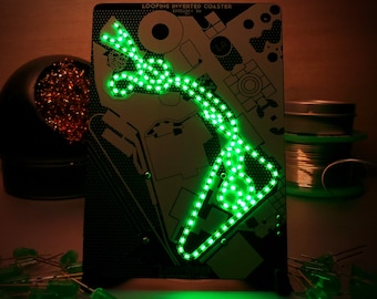 May include: A circuit board with the text "LOOPING INVERTED COASTER" and a green LED light design. The design resembles a roller coaster track. Additional green LEDs and a soldering iron are visible.