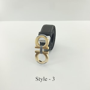 以下が含まれることがあります： ダブルGのデザインが特徴の、ゴールドカラーのバックルが付いた黒いレザーベルト。 ベルトは丸められており、その質感と金属製のバックルが際立っています。 テキスト「Style - 3」が下に表示されています。