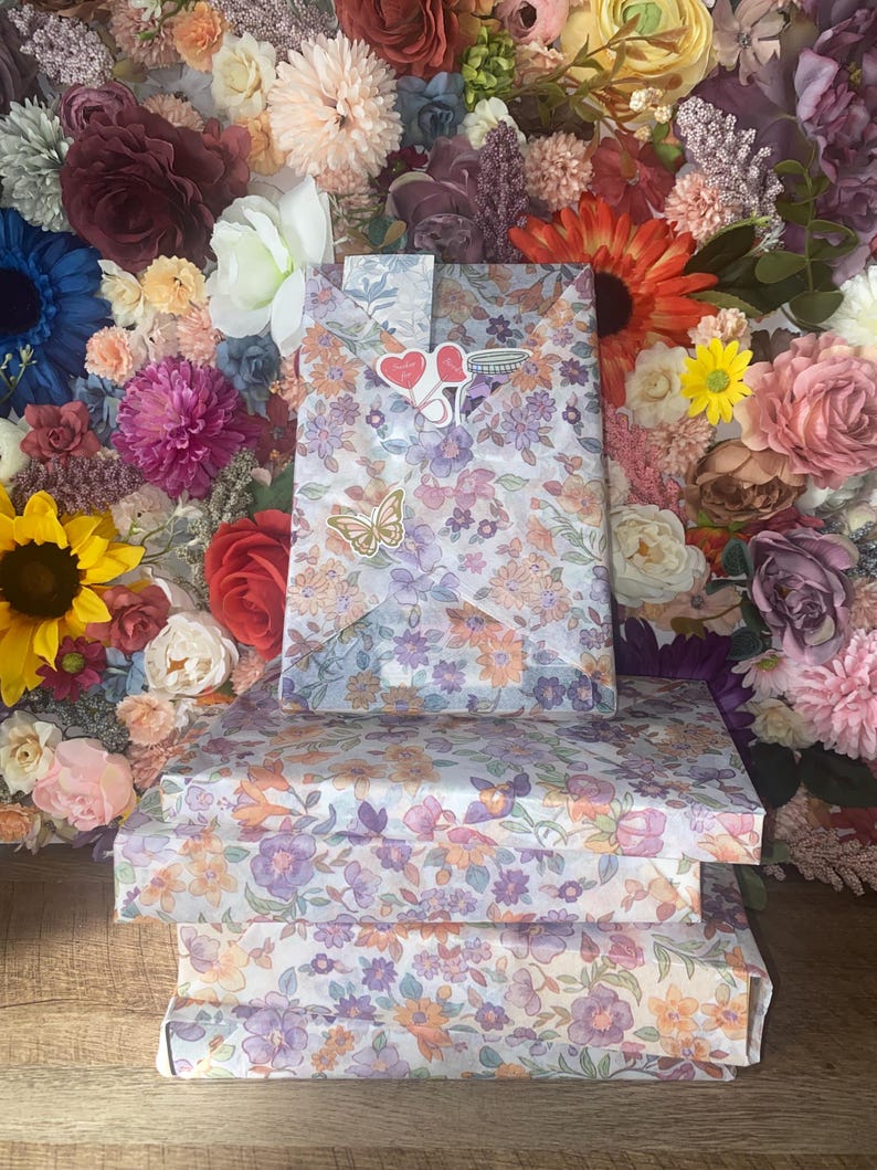 Puede incluir: Tres cajas de regalo envueltas en papel con estampado floral con flores moradas, naranjas y blancas. Un cuarto regalo est&aacute; envuelto en el mismo papel y cubierto con pegatinas de coraz&oacute;n y una pegatina de mariposa. El fondo es una pared de flores coloridas.