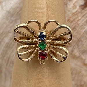 Puede incluir: Un anillo de mariposa de oro con piedras preciosas rojas, verdes y azules.