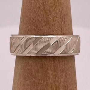 May include: A silver wedding band with a textured, diagonal pattern.